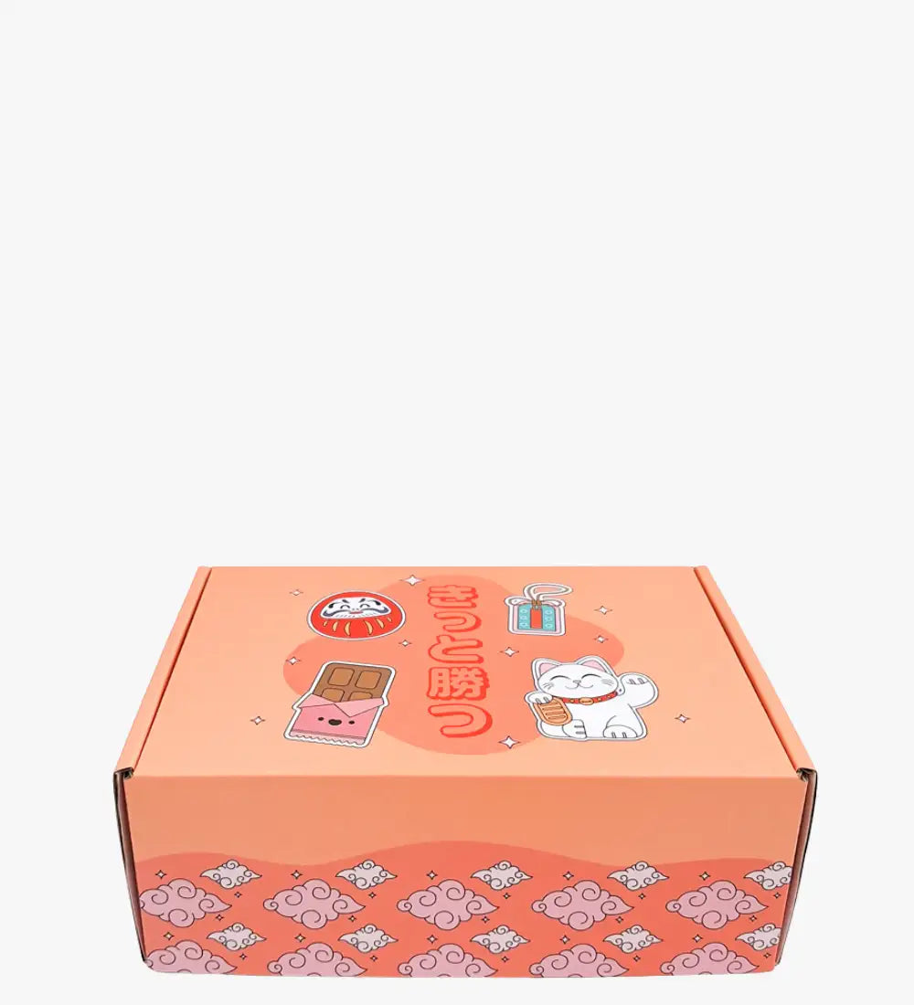 Korallenfarbene Kartonbox mit niedlichen japanisch inspirierten Illustrationen, einschließlich einer weißen Glückskatze, eines Daruma-Balls und Schokoladenriegel-Designs.
